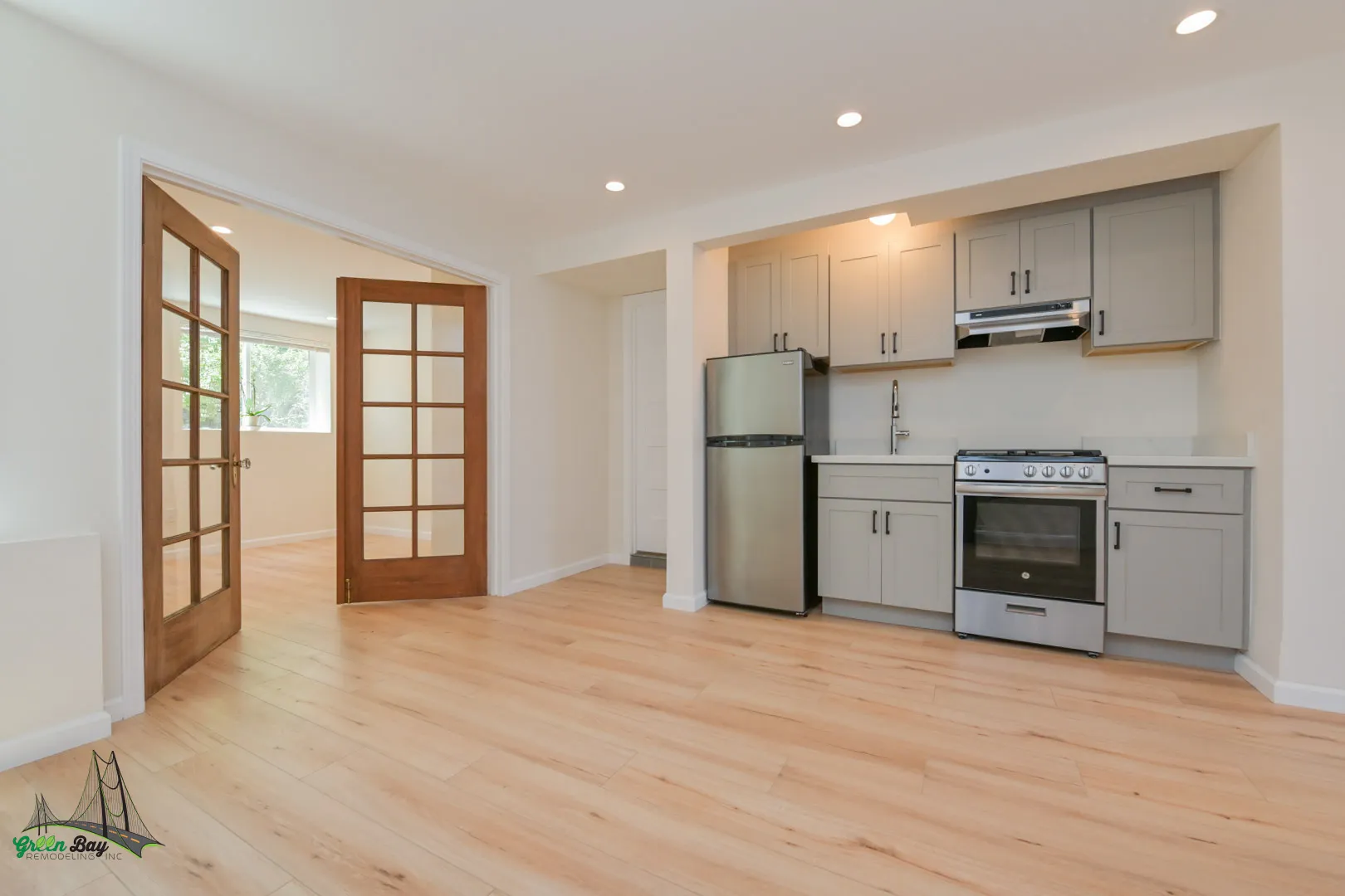 Modern ADU conversion featuring light wood flooring, gray shaker cabinets, stainless steel appliances, and French doors that open to a bright living area in San Jose, CA.