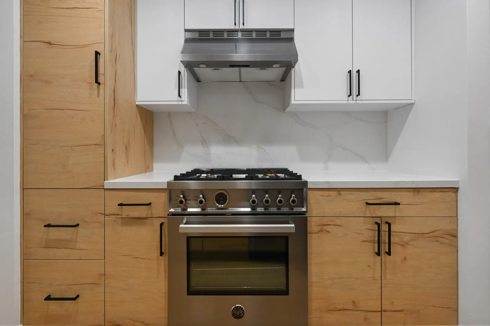 Modern kitchen from a full home remodel in Mariner, Corte Madera featuring natural wood cabinetry, white quartz countertops, and a stainless steel gas range.